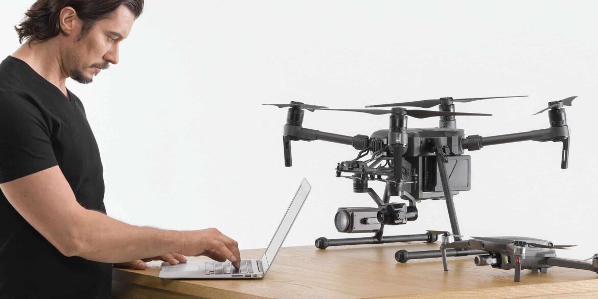 Man operating a laptop beside two advanced drones on a wooden table.