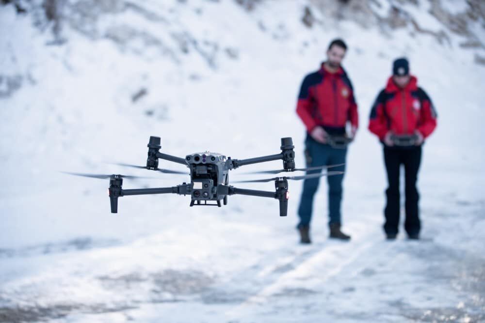 A drone in flight with two operators using remote controls in a snowy environment.