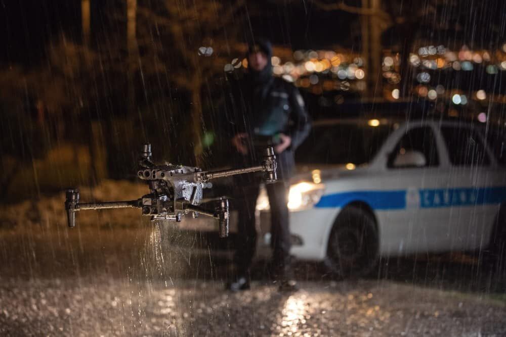 Bewakingsdrone tijdens de vlucht met een politieagent en een politievoertuig in de regen.