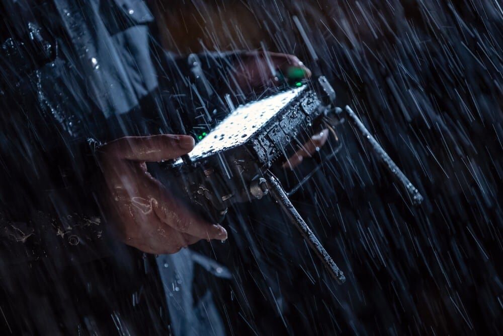 A person holding a drone in heavy rain, with water drops visible on the device.